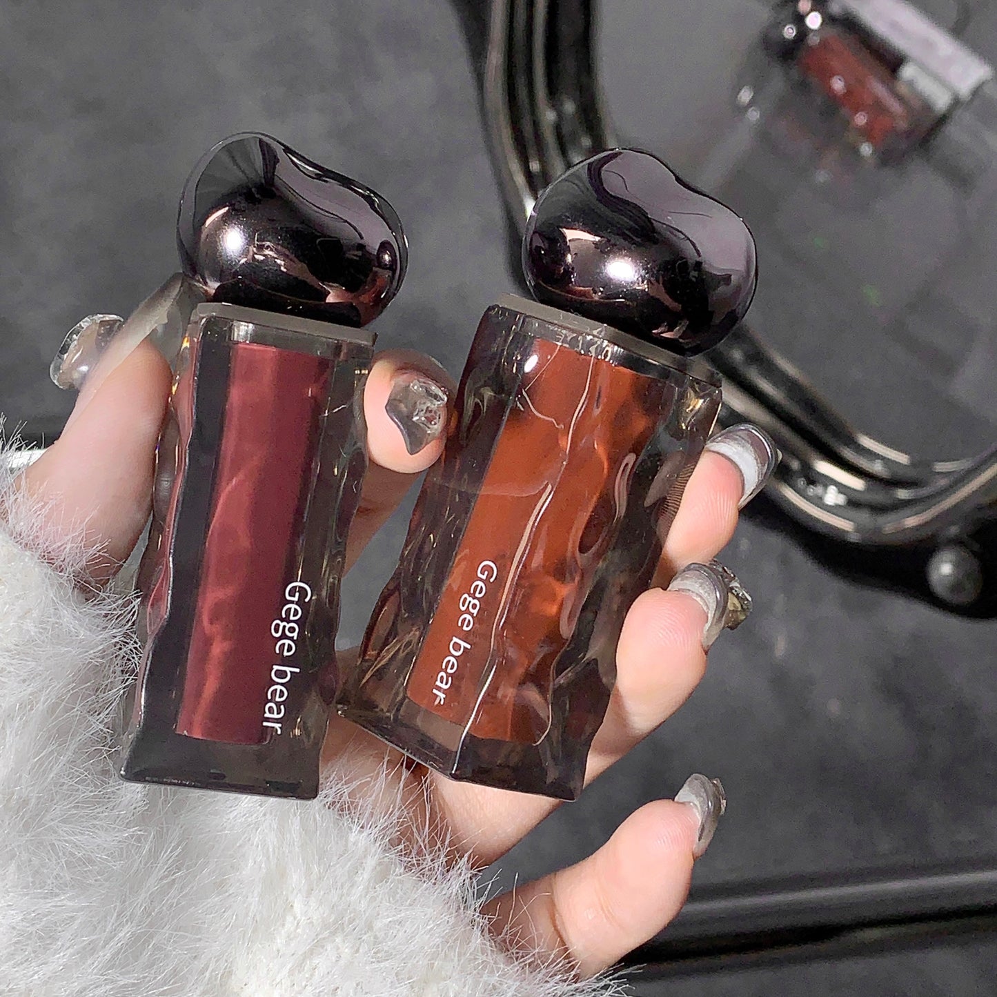 Two lip glosses held by a hand with a blurred background