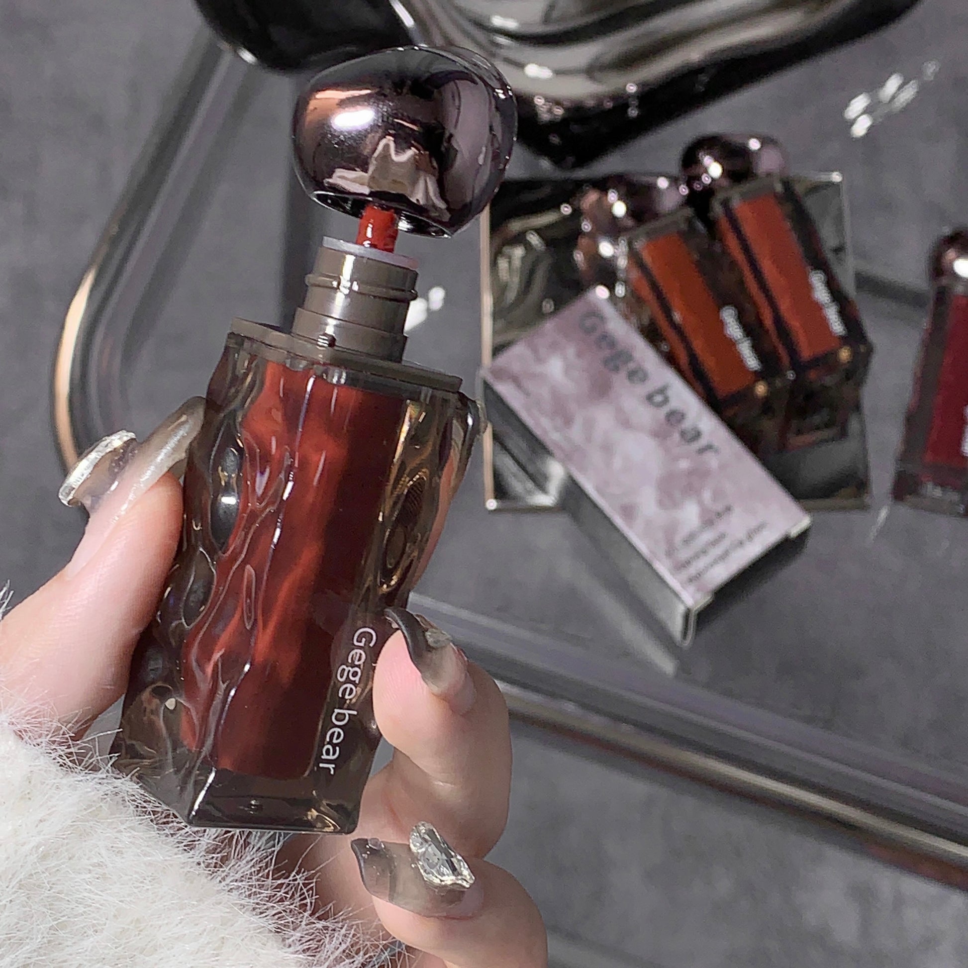 Hand holding a perfume bottle labeled 'Geese bear' with a blurred background