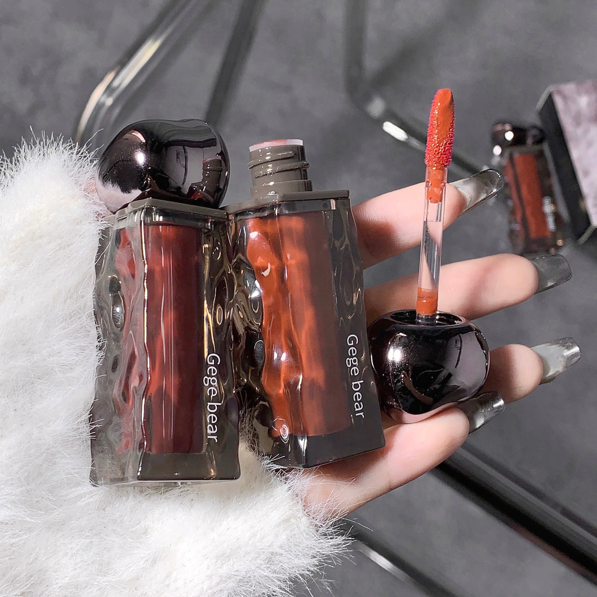 Lip gloss with packaging held by a hand on a textured surface