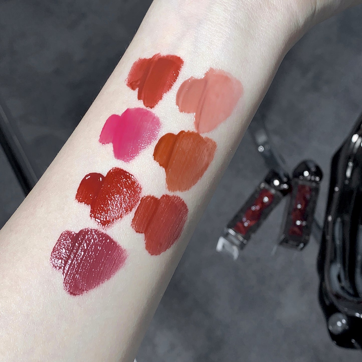 Lipstick swatches on a person's arm with lipsticks below