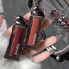 Two lip glosses with 'Gege bear' branding held in a hand against a blurred background.