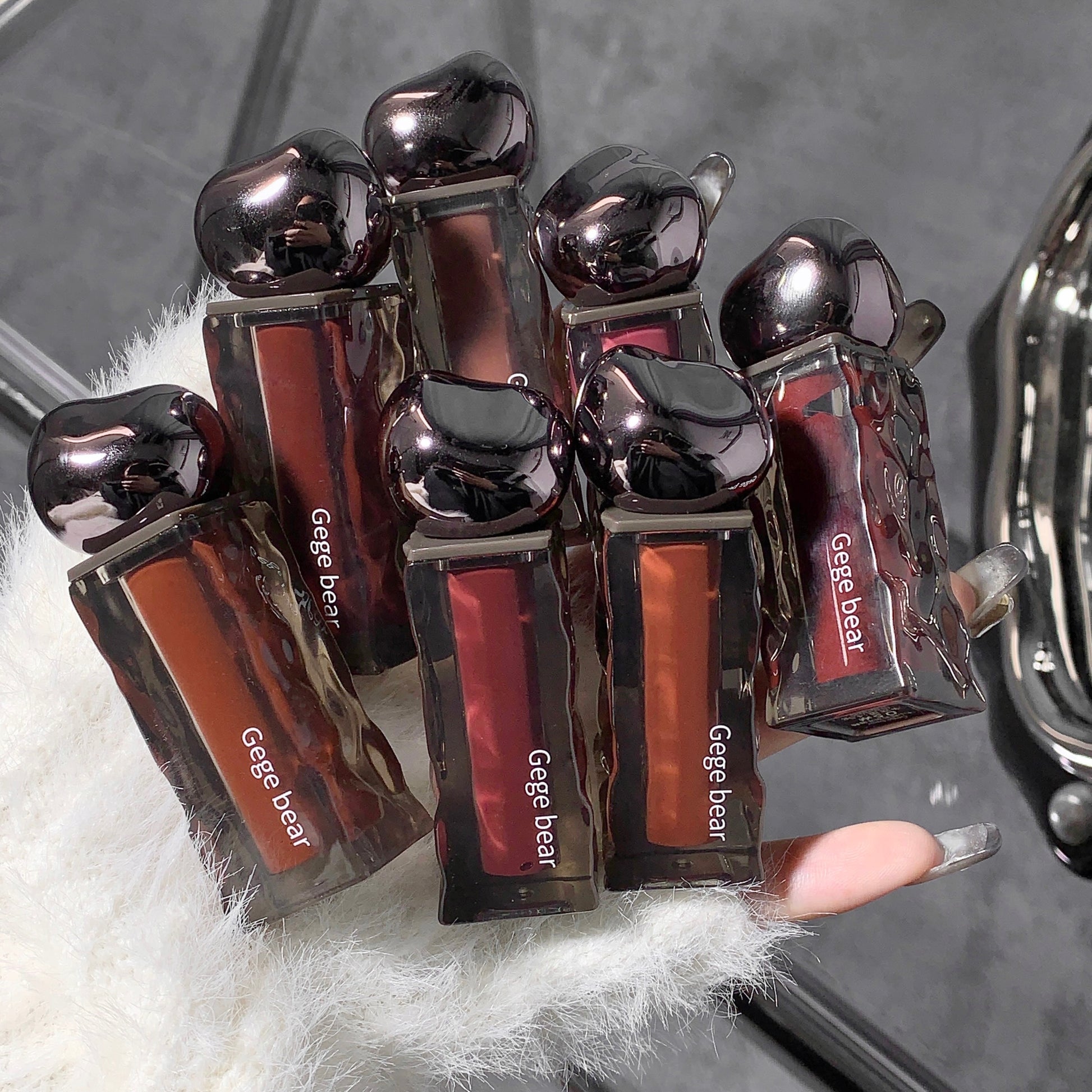 Set of Gege bear lip glosses held by a hand with a textured background
