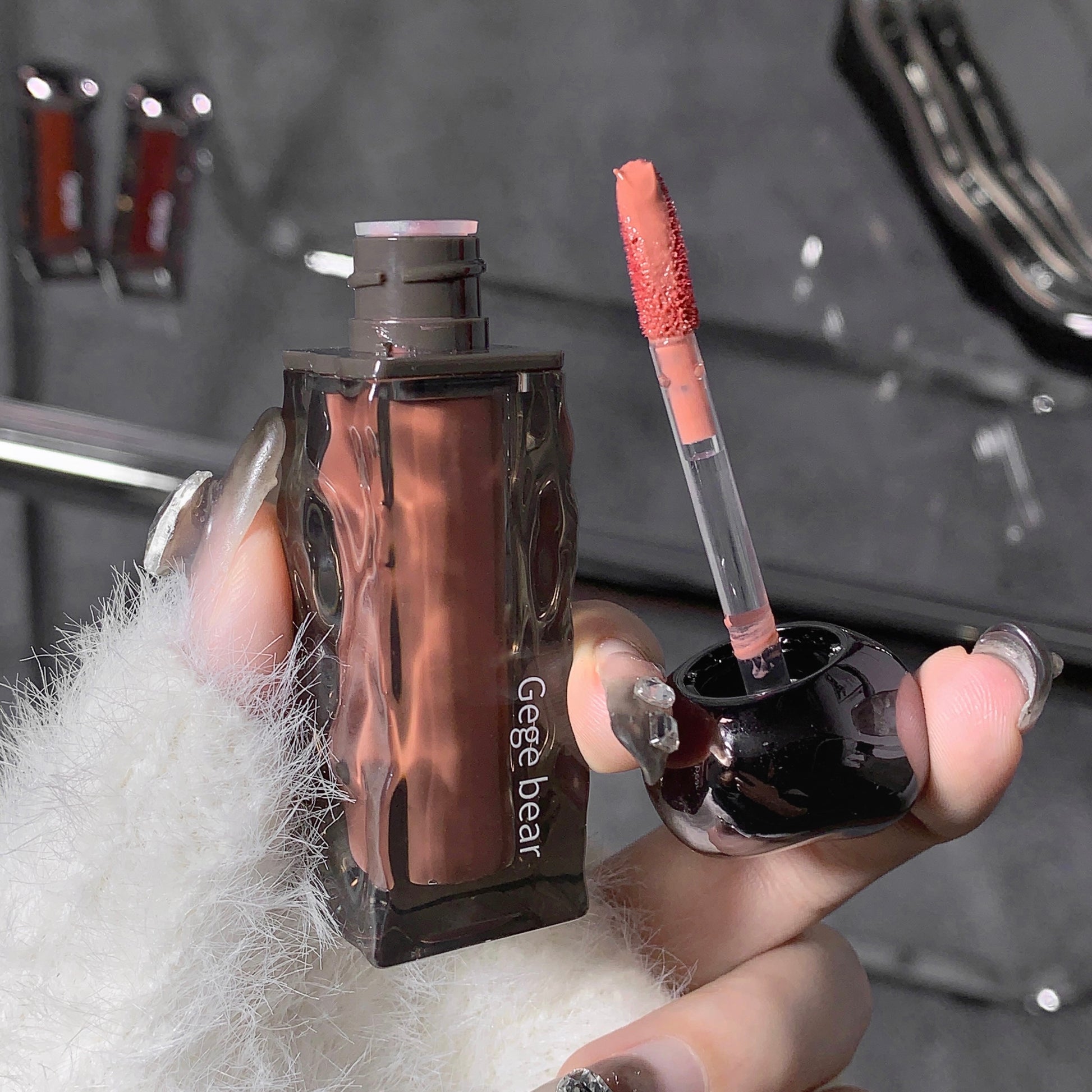 Lip gloss and its packaging held by a hand with a blurred background