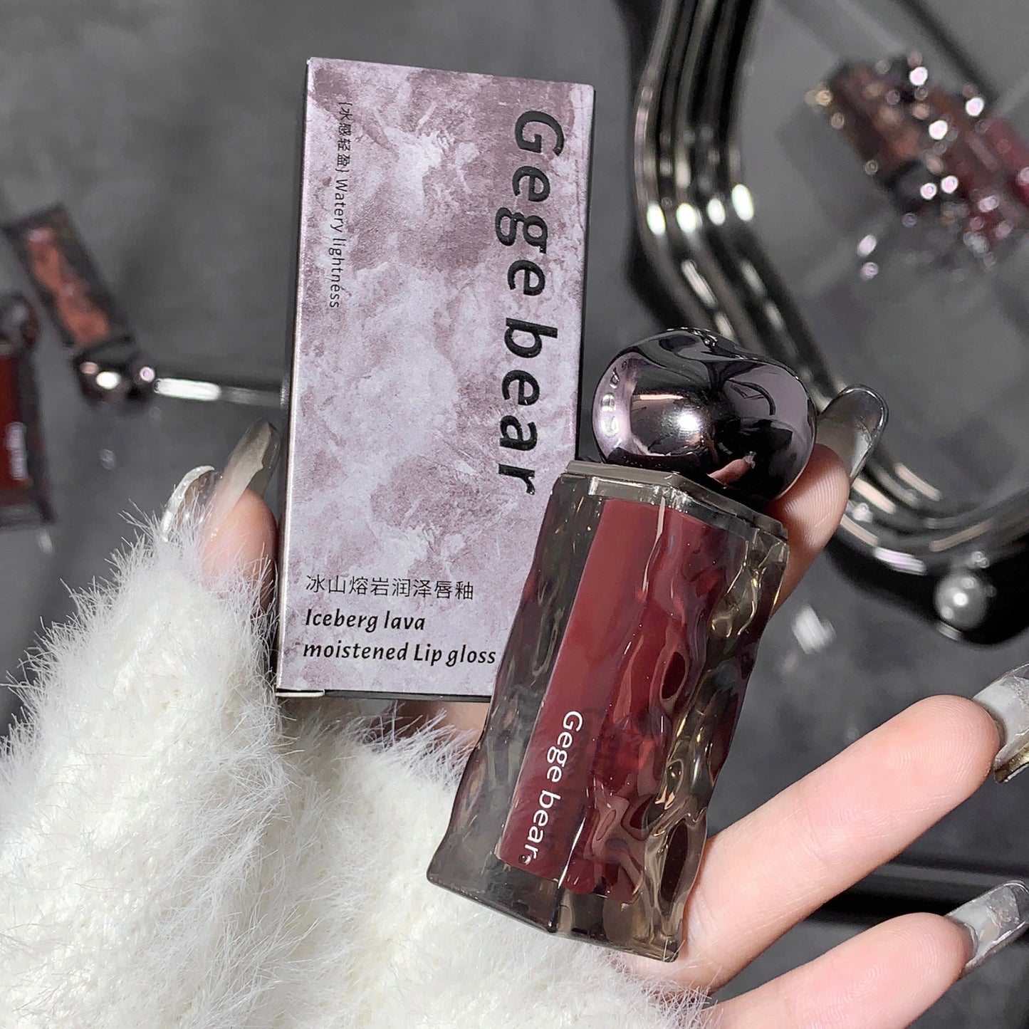 Lip gloss with packaging labeled 'Gegebear' held by a hand against a blurred background.