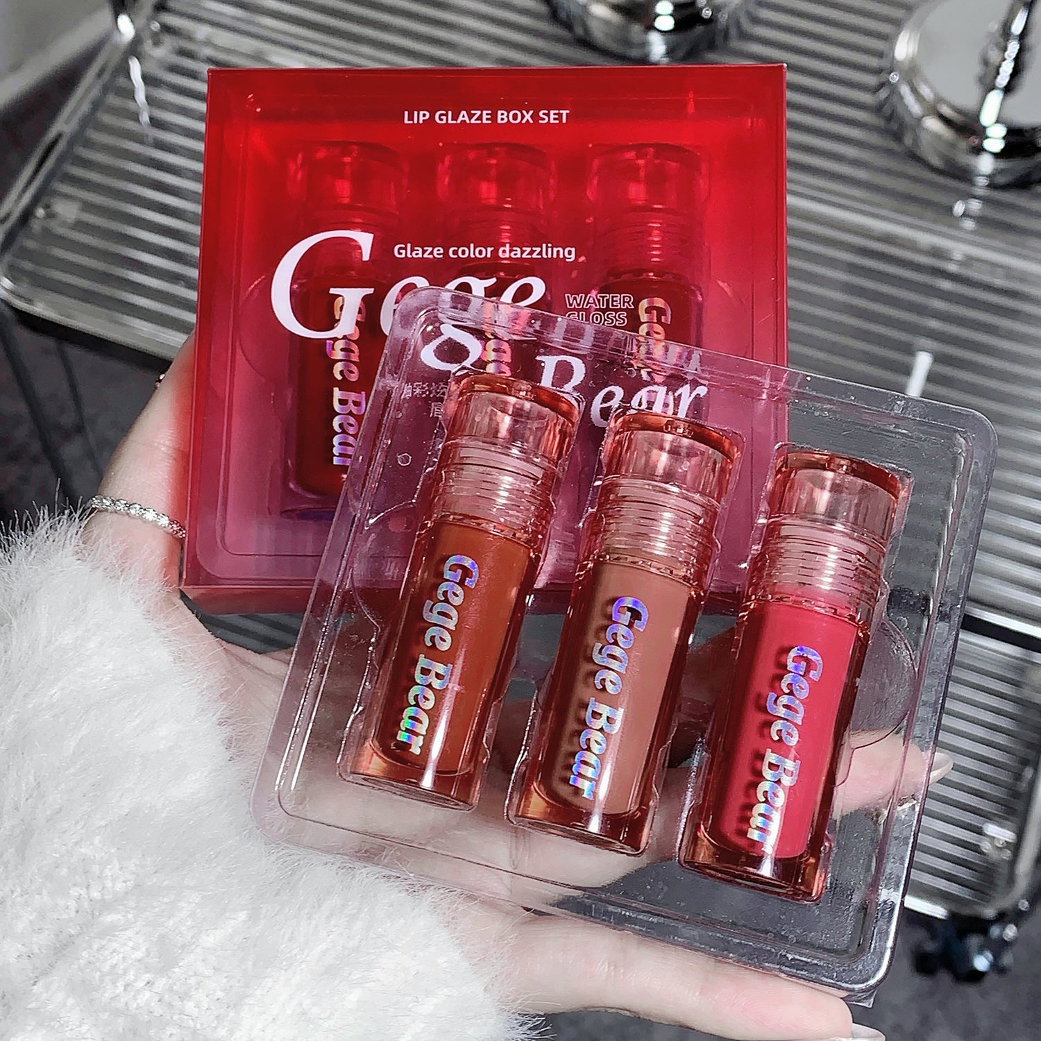 Set of lip glosses in clear packaging with 'Gige Bear' branding, held by a person.