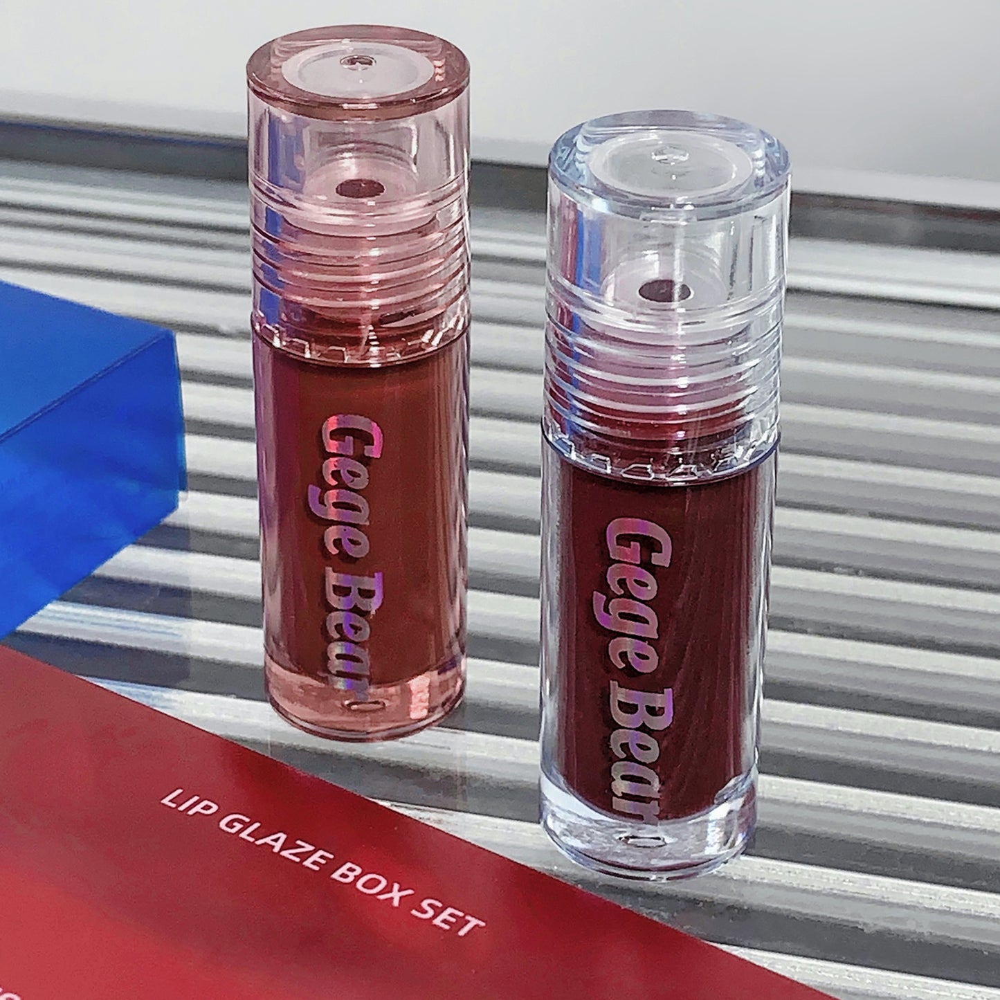 Two lip glosses from Gege Bear with a box set label on a striped background