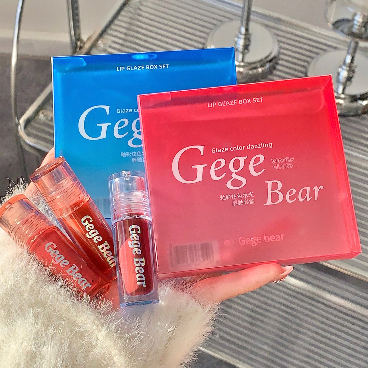 Gege Bear lip gloss set with red and blue packaging held by a person.