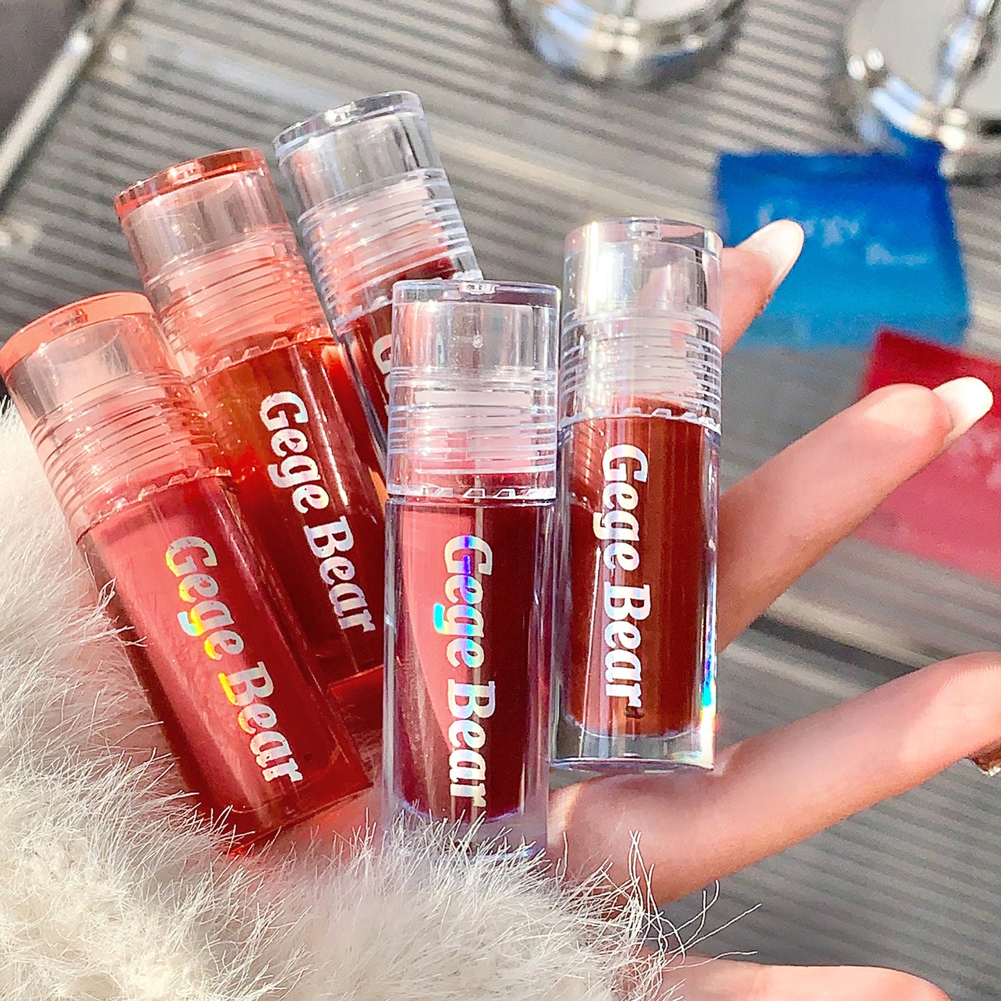 Multiple Gege Bear lip glosses held by a hand with a blurred background