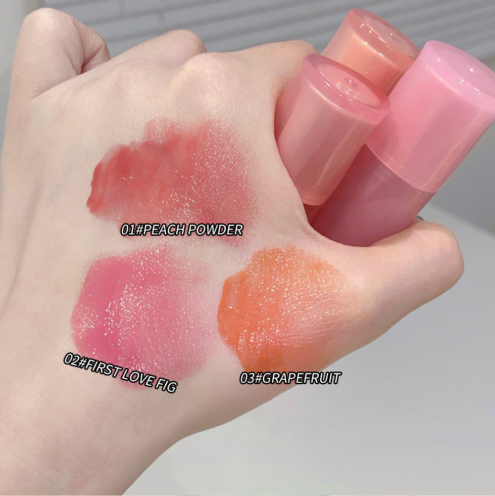 Three lip balm tubes with swatches on a hand labeled 'Peach Powder', 'First Love Fig', and 'Grapefruit'.