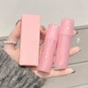 Pink skincare product set held by a hand against a neutral background