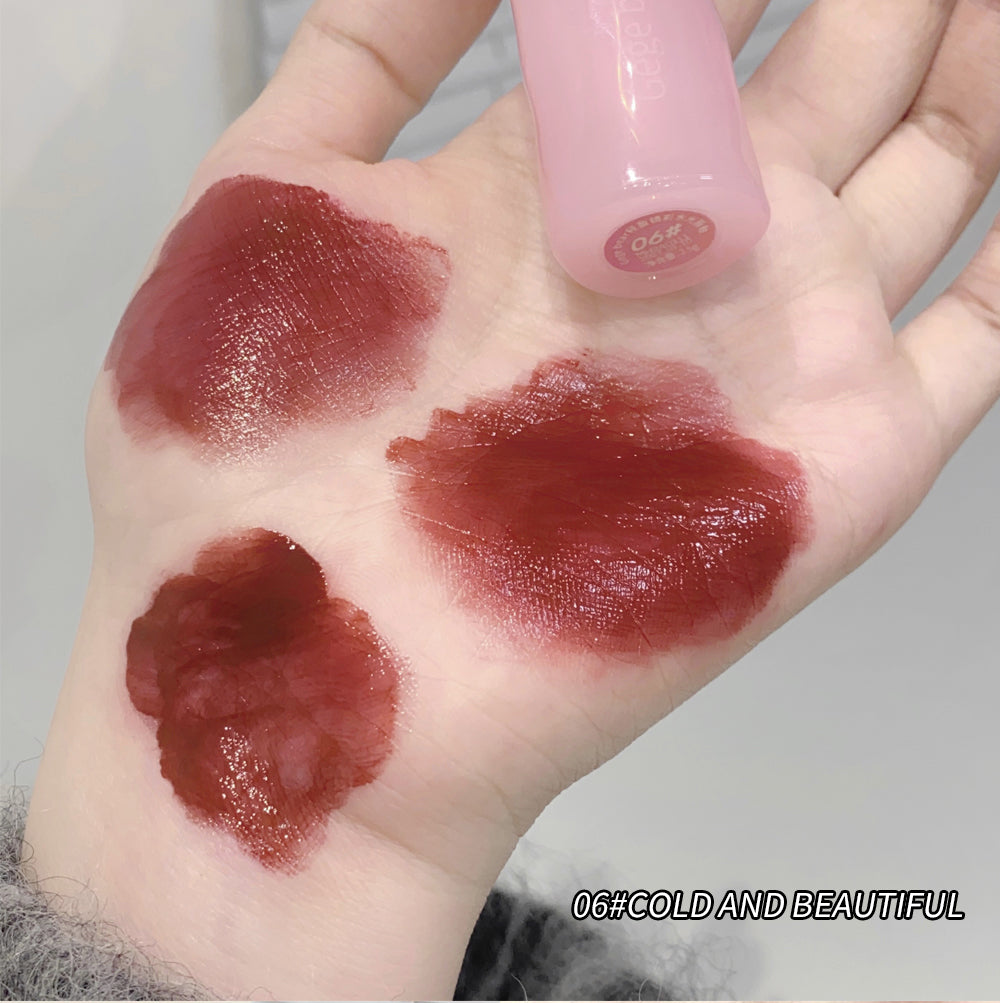 Hand with three different shades of red lipstick applied, with a pink lip gloss container.