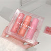 Three lip glosses in pink and peach shades in a clear packaging held by a hand.