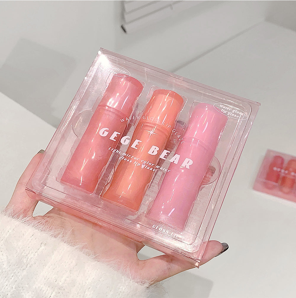 Three lip glosses in pink and peach shades in a clear packaging held by a hand.