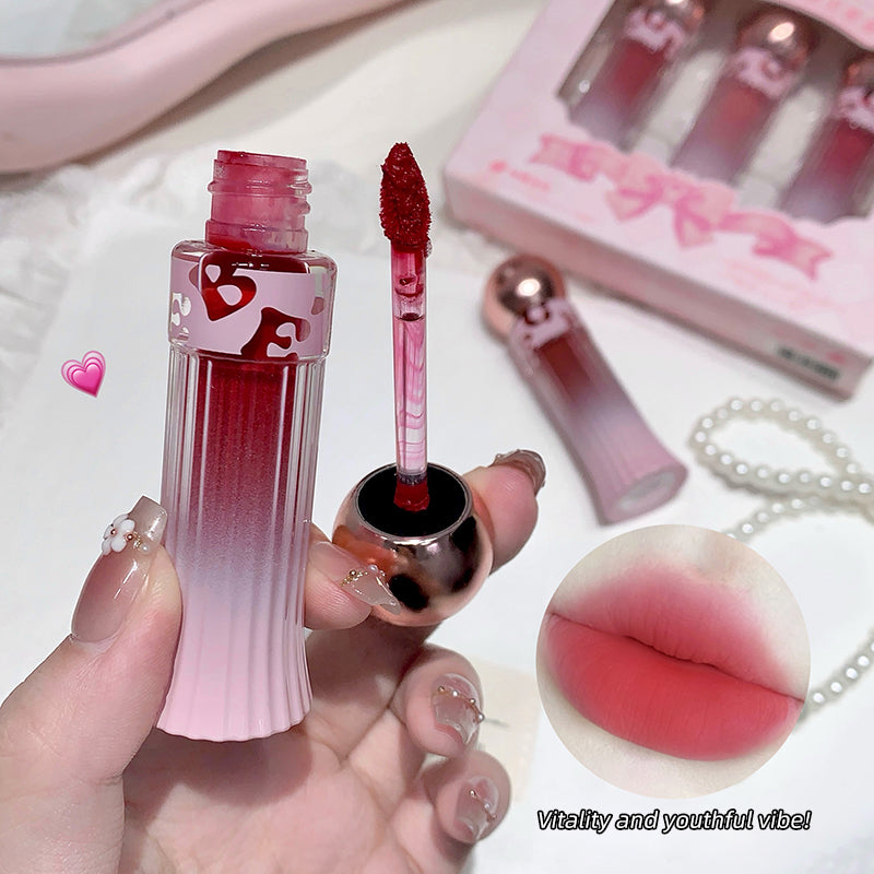 Pink and red gradient lip gloss held by a hand with a matching box in the background.