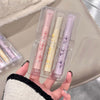 Three lip glosses in clear packaging held by a hand against a neutral background