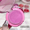 Pink makeup compact with mirror, held by a hand, on a blurred background.