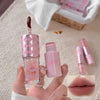Pink lip gloss with applicator held by a hand, close-up on a textured surface.
