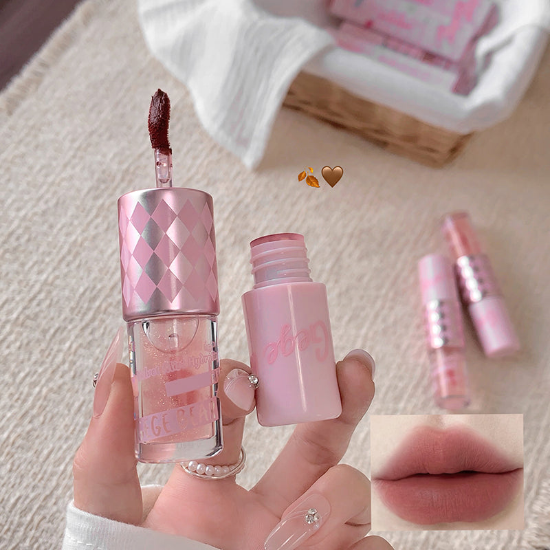 Pink lip gloss with applicator held by a hand, close-up on a textured surface.