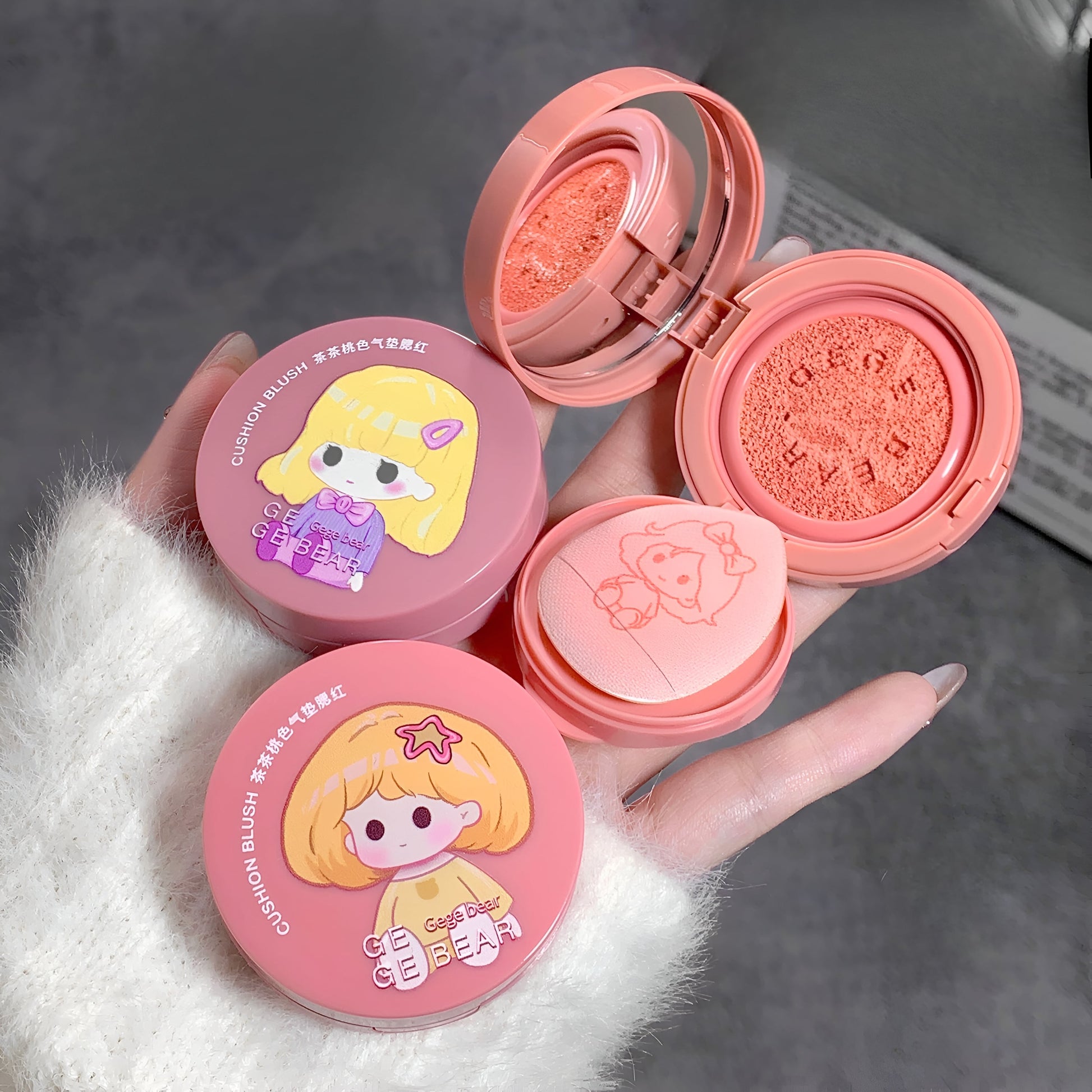 Pink makeup compact with cartoon character design held by a hand on a gray background
