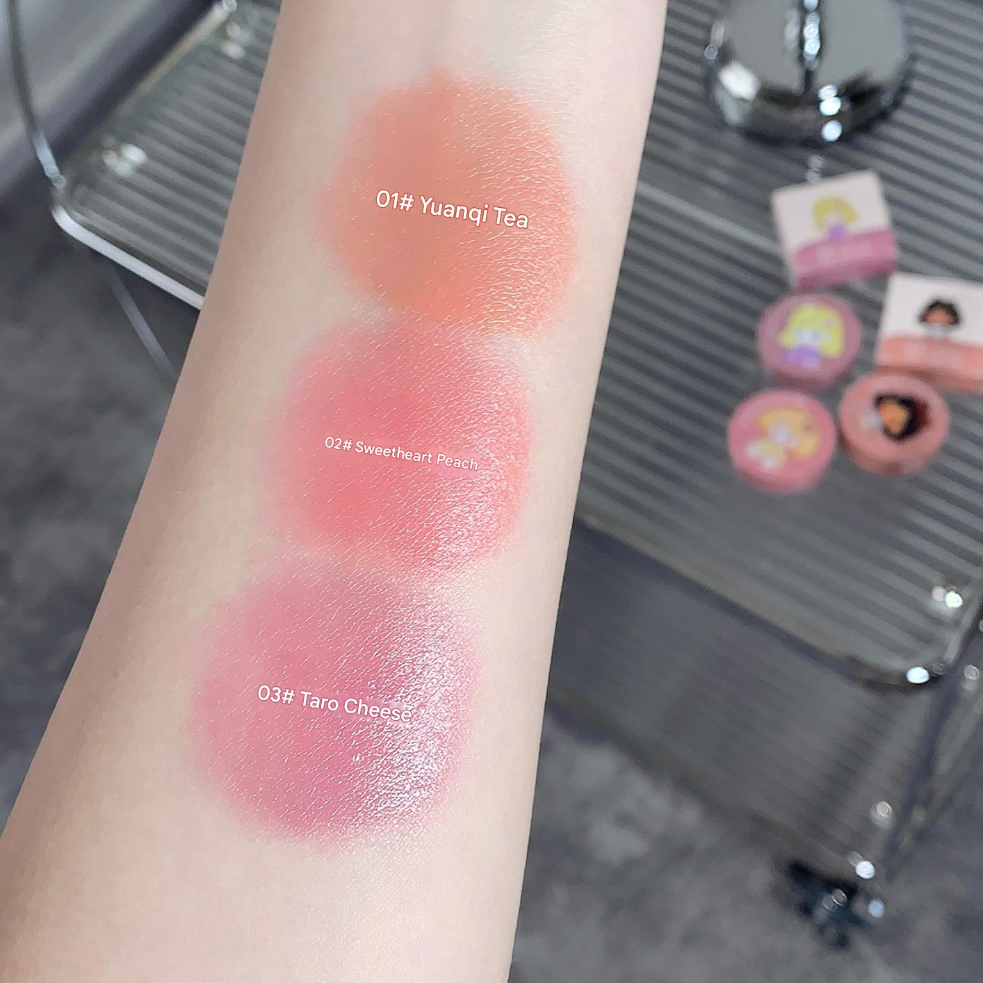 Lipstick swatches on a person's arm with labeled colors against a blurred background.