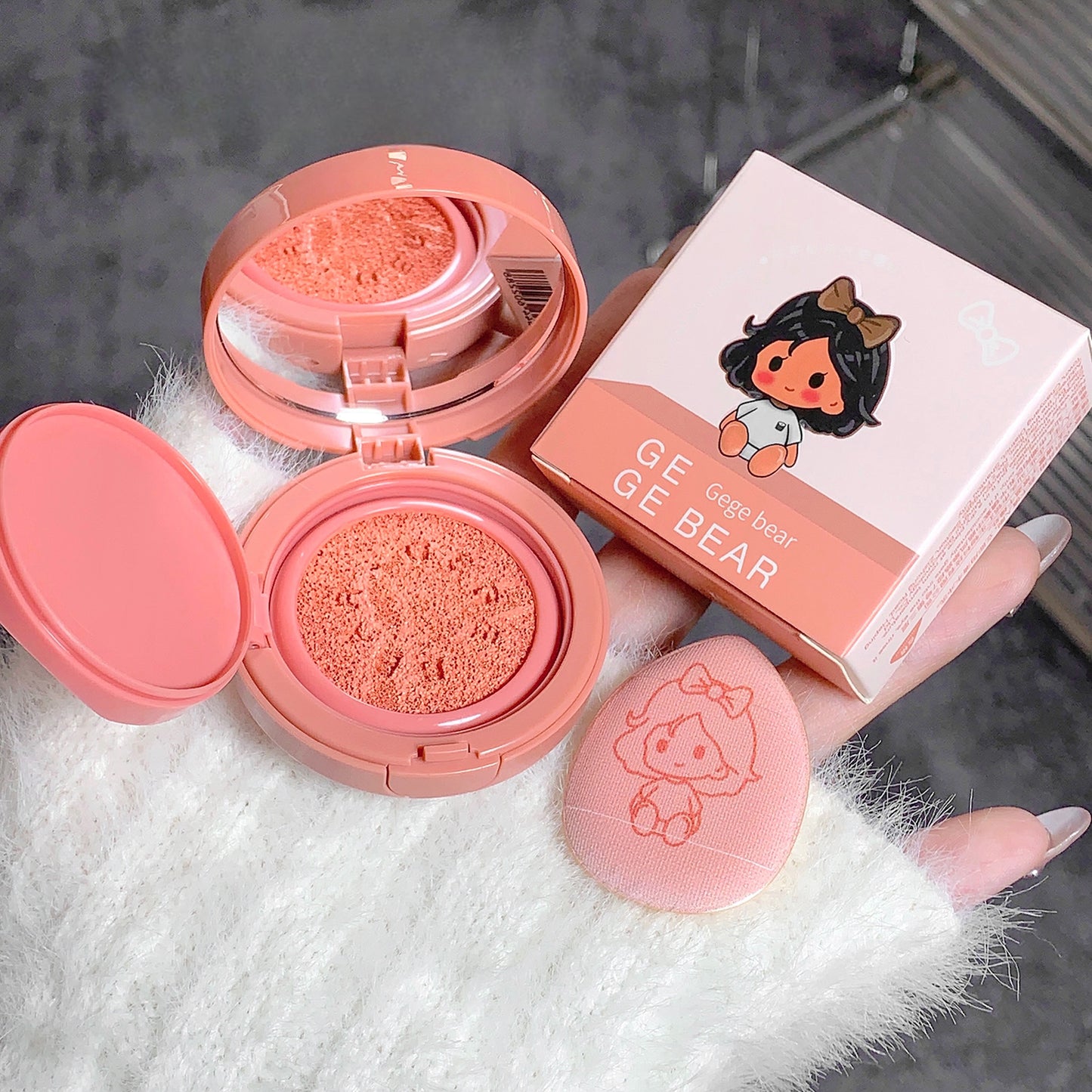 Pink compact makeup with open lid showing blush, closed box, and small round item on a textured surface.