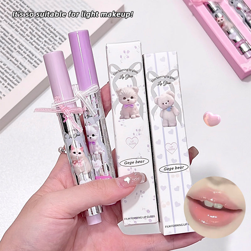 Lip gloss with bear design packaging held by a hand, on a light background.