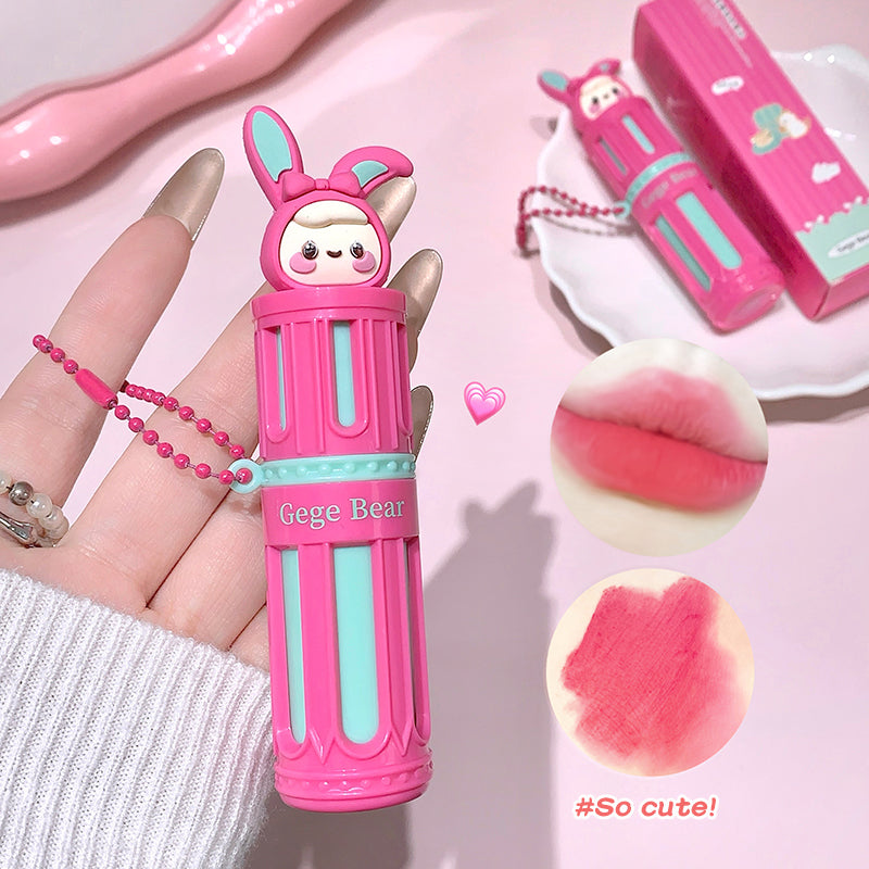 Pink lip balm with bear design held by a hand, on a pink background.