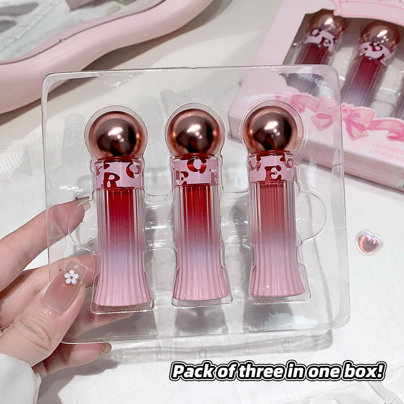 Pack of three lip glosses in a clear plastic case held by a hand.