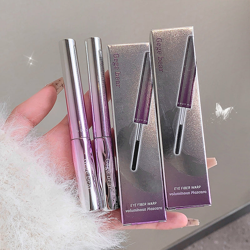 Two silver and purple mascara tubes with their packaging held by a hand against a neutral background.