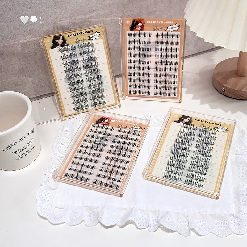 Four trays of false eyelashes on a white surface with a mug and lace doily.