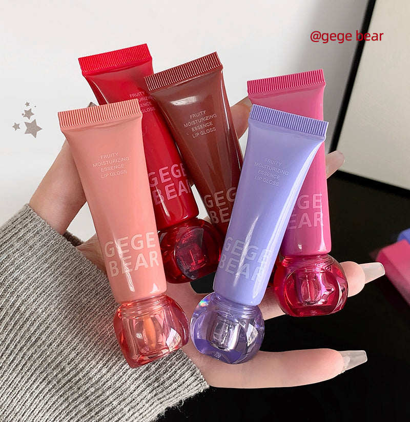 Hand holding four lip gloss tubes with 'GEGE BEAR' branding against a neutral background.