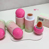 Set of pink and green cosmetic products with a brush on a white surface.