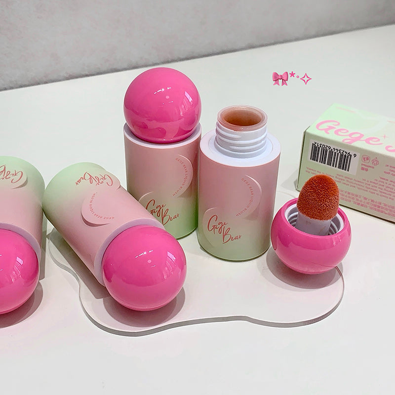 Set of pink and green cosmetic products with a brush on a white surface.