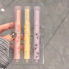 Three lip balms in a clear packaging with floral designs held by a hand.