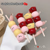 Colorful lip mud on sticks with cartoon faces held by a hand against a neutral background