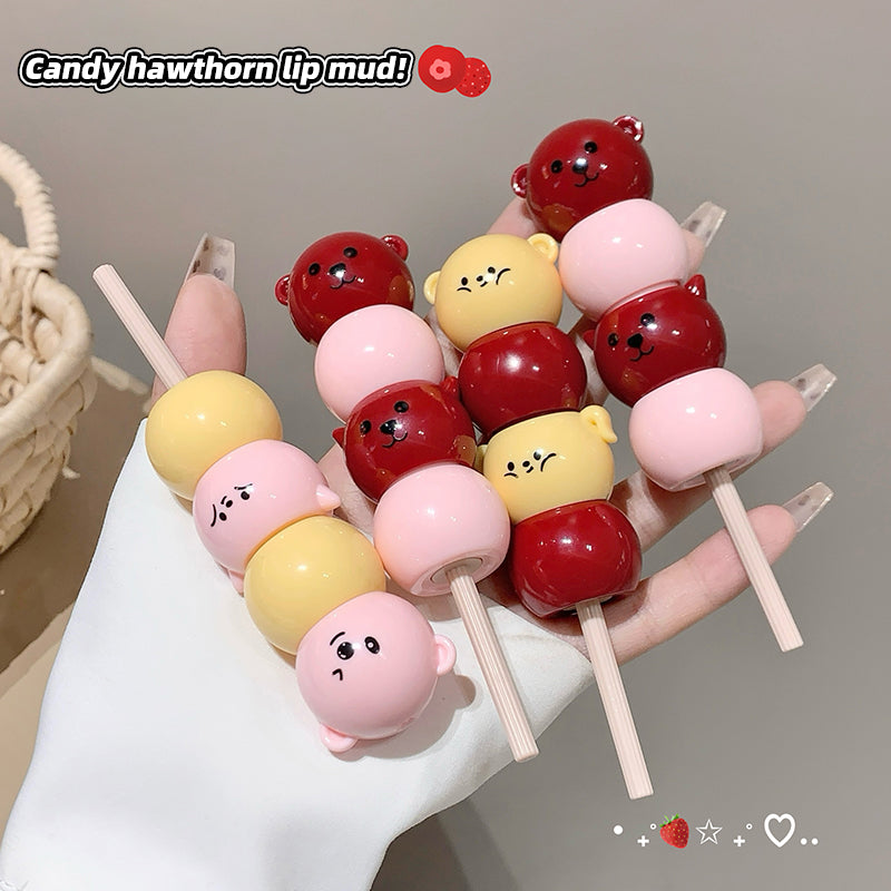 Colorful lip mud on sticks with cartoon faces held by a hand against a neutral background