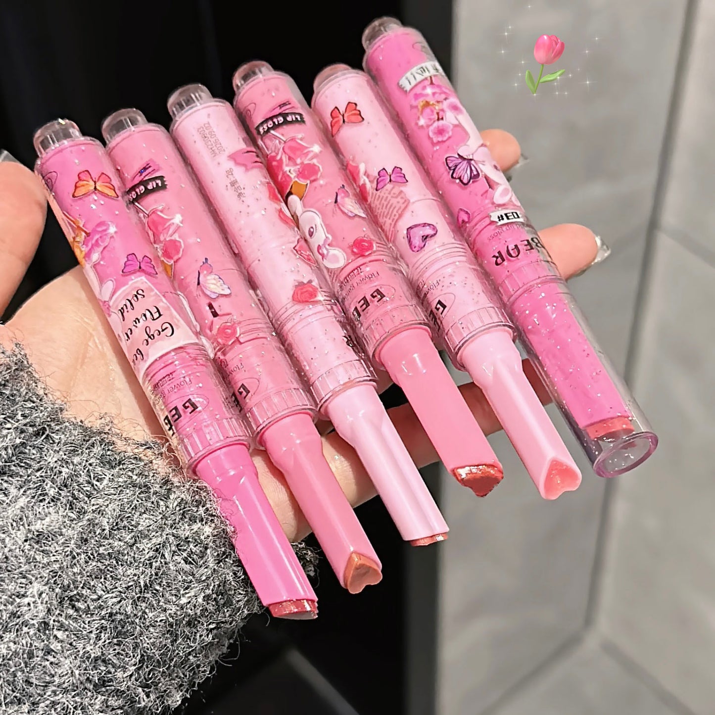 Set of pink pens with cartoon designs held by a hand against a neutral background