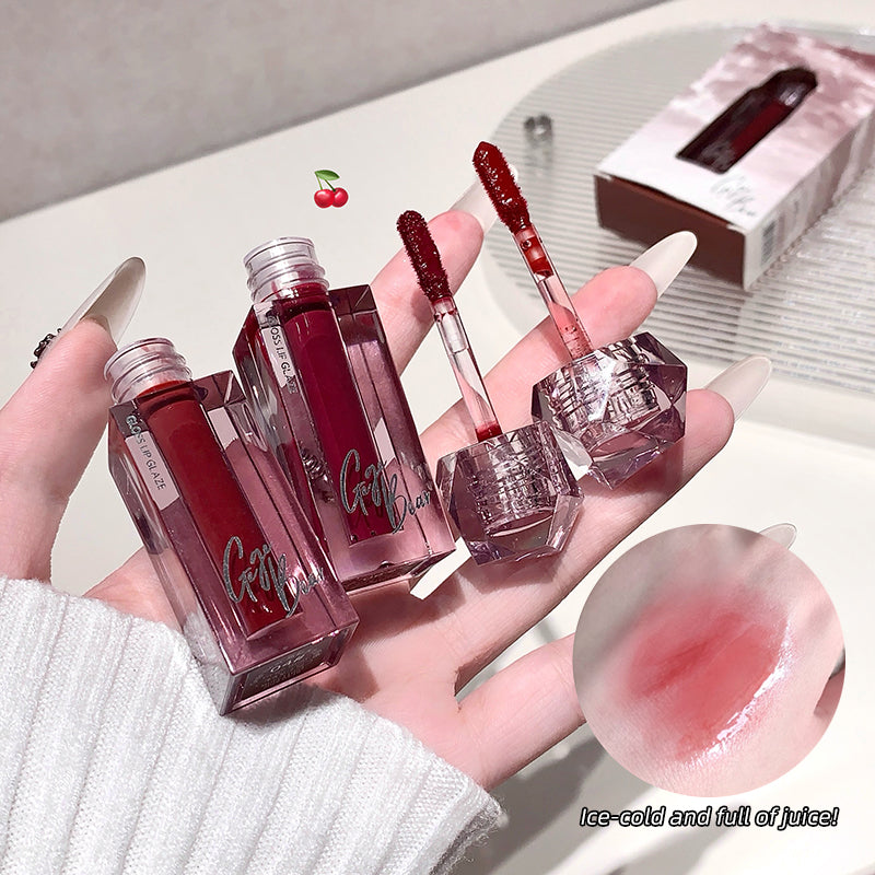 Hand holding four lip glosses with a cherry on top, set against a neutral background.