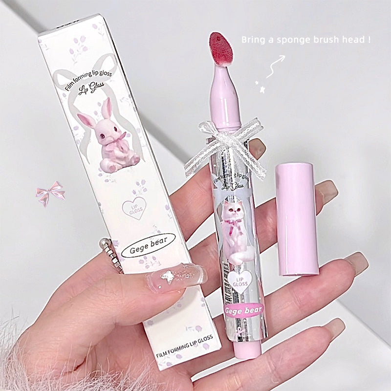 Pink lip gloss with bunny design held by a hand on a light gray background