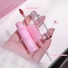 Pink lip gloss and applicator held by a hand on a white surface