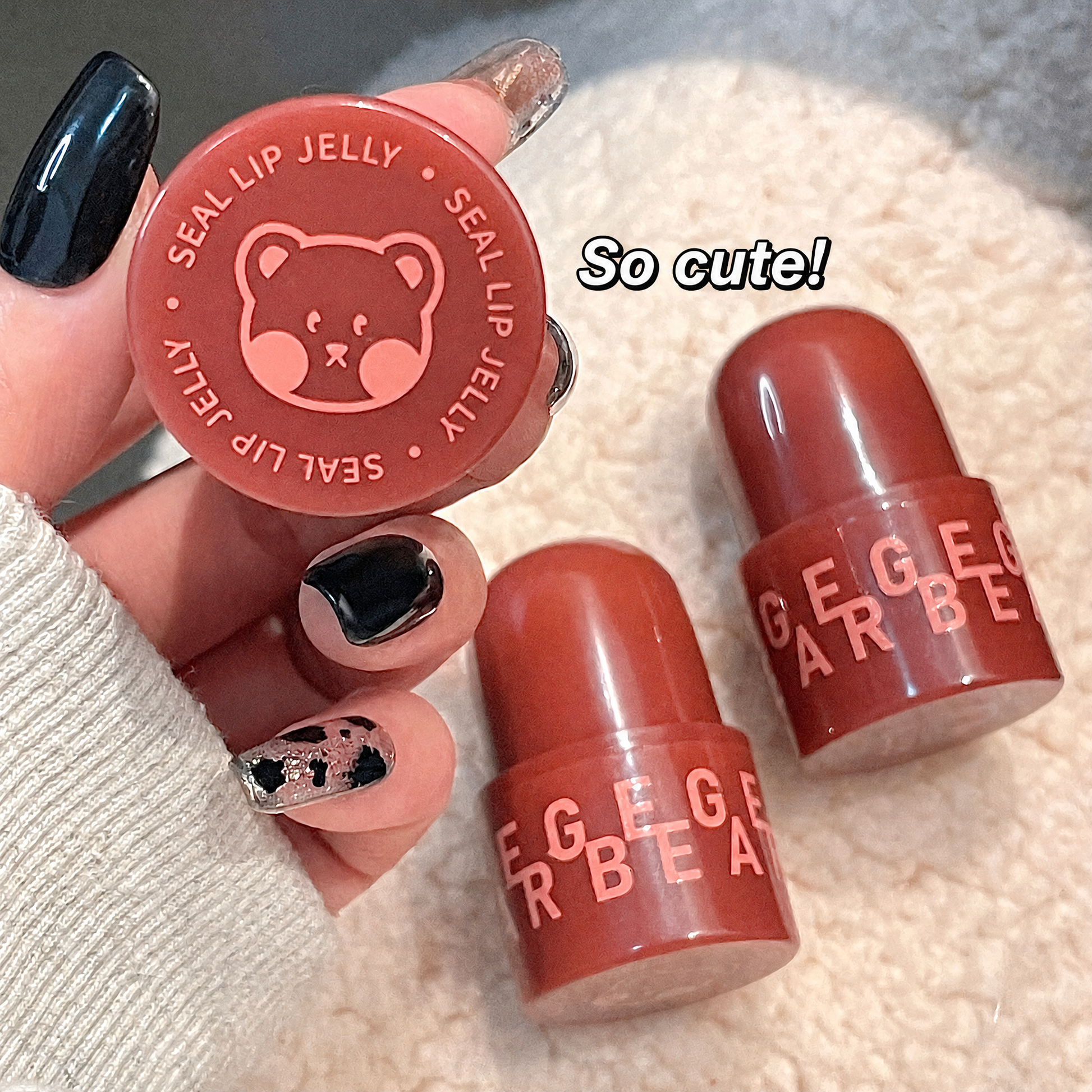 Two red lip glosses with 'GEGER BEAT' branding held by a hand with black nail polish.