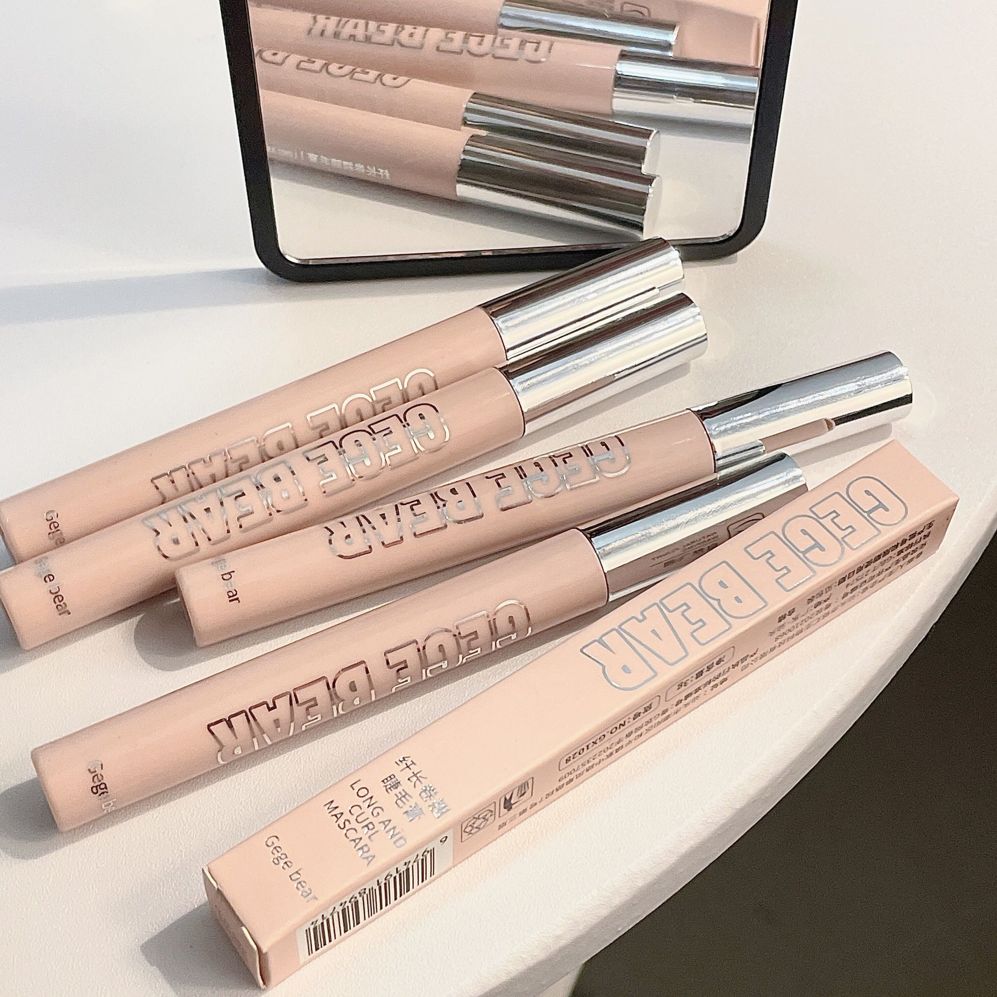 Three lip glosses with their packaging on a light surface, one of which is open.