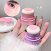 Two pink Gege bear makeup sponges held by a hand with a close-up of an eye.