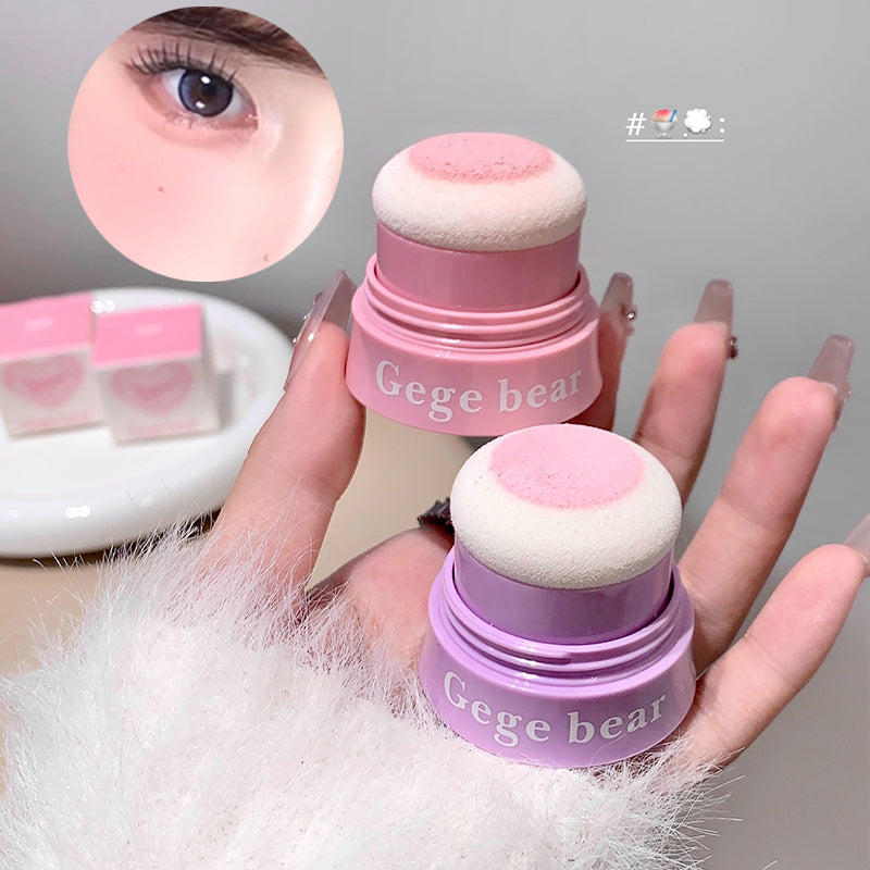 Two pink Gege bear makeup sponges held by a hand with a close-up of an eye.
