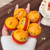 Hand holding a set of cute yellow and red toy buns with cartoon faces on a wooden surface.