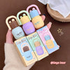 Set of colorful Gege Bear lip balms and packaging held by a hand on a brown background.