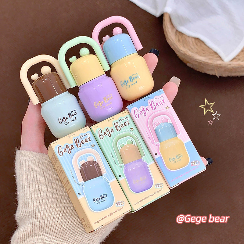 Set of colorful Gege Bear lip balms and packaging held by a hand on a brown background.