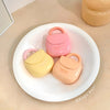 Three small, pastel-colored cases with handles on a white plate.