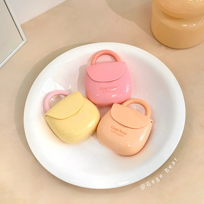 Three small, pastel-colored cases with handles on a white plate.