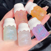 Five small lip gloss bottles with colorful labels held in a hand against a dark background.